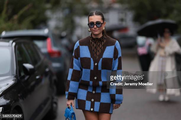 Lina Uhrig seen wearing Corlin Eyewear black sunglasses with blue transparent lenses, gold earrings, Gestuz brown / black triangle print pattern...