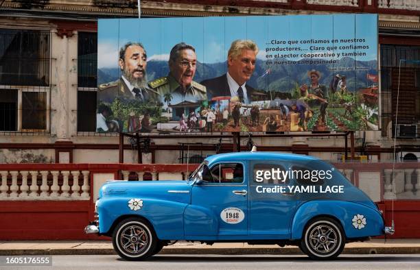 An old American car passes near a poster of Cuban late leader Fidel Castro , Former President Raul Castro and current President Miguel Diaz-Canel in...