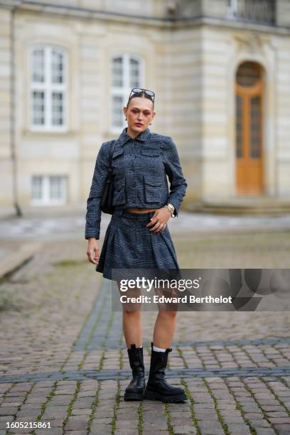 Guest wears black sunglasses, a dark gray checkered print pattern buttoned cropped jacket, a matching dark gray checkered print pattern pleated /...