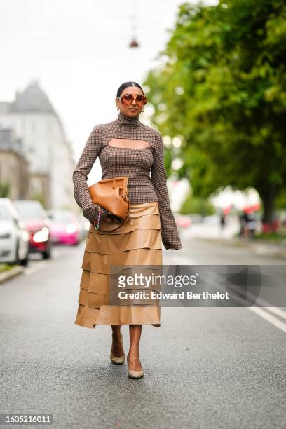 Guest wears camel sunglasses, a brown and beige checkered print pattern long sleeves / cut-out chest top, a camel shiny leather puffy handbag from...