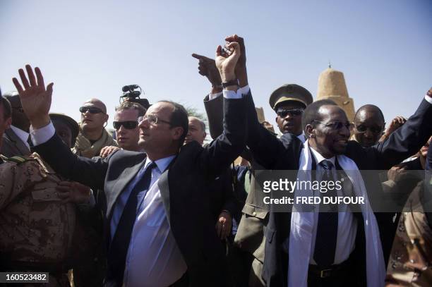 France's President Francois Hollande flanked by Mali's interim president Dioncounda Traore , wave as Hollande arrives at the airport of Timbuktu, the...