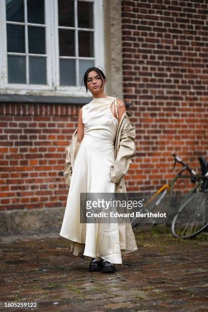 Guest wears a white latte silk high neck / asymmetric shoulder long dress, a beige long trench coat, a black shiny leather handbag, black shiny...
