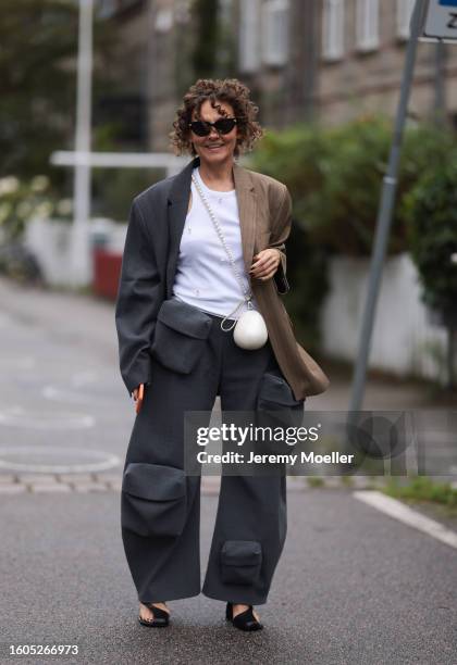 Guest wears Bottega Veneta black sunglasses, white cotton tank top with stitched beads, two colored grey / brown striped blazer jacket, matching grey...