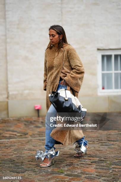 Guest wears a brown sheep long coat, a black leather and white fabric bicolored pattern handbag from Loewe, blue denim large pants , silver shiny...