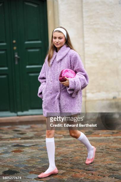 Guest wears a white large headband, a pale purple sheep fur long coat, a neon pink ruffled silk handbag, white socks, pale pink suede ballerinas ,...
