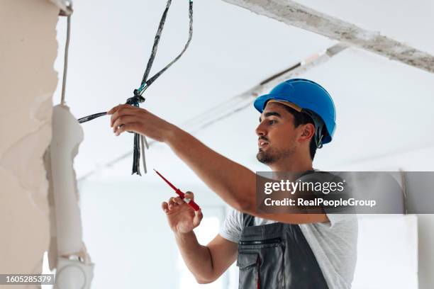 die konzentrierte anstrengung des jungen arbeiters verbessert die wohnungsdecke bei der renovierung - broken lamp stock-fotos und bilder