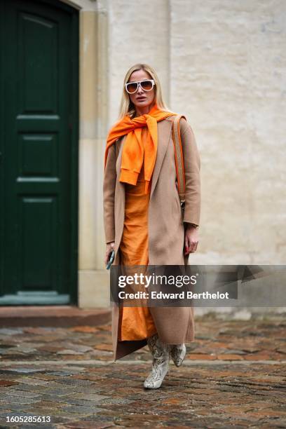 Guest wears white sunglasses from Louis Vuitton, a neon orange wool pullover knot at the shoulder, an orange long silk dress, a beige wool long coat,...