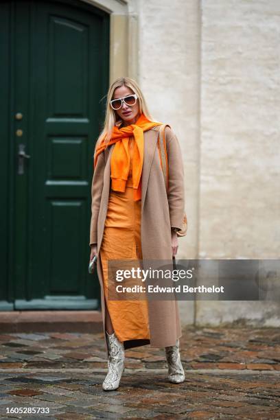 Guest wears white sunglasses from Louis Vuitton, a neon orange wool pullover knot at the shoulder, an orange long silk dress, a beige wool long coat,...
