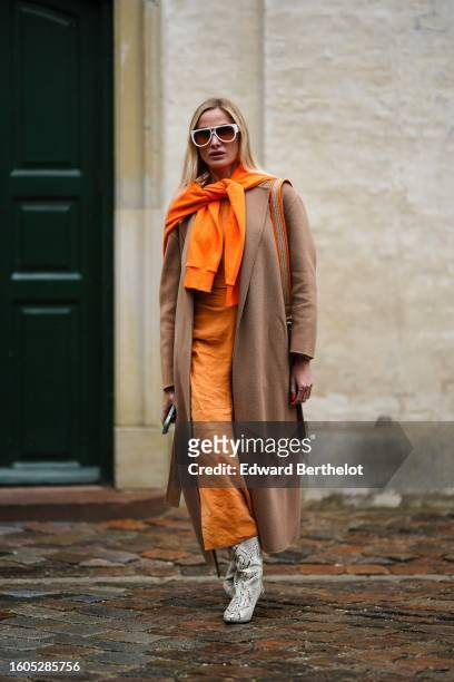 Guest wears white sunglasses from Louis Vuitton, a neon orange wool pullover knot at the shoulder, an orange long silk dress, a beige wool long coat,...