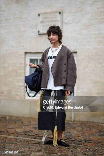 Guest wears a silver large chain necklace, a white pearls necklace, a white with black logo print pattern t-shirt from Jil Sander, a dark gray...