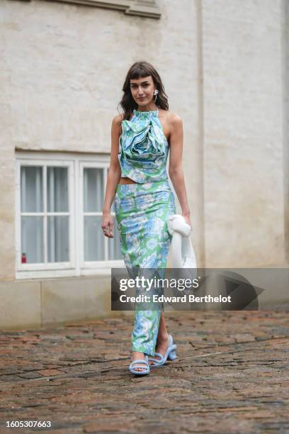 Mari Alexander wears silver large pendant earrings, a white / blue / green print pattern silk halter-neck tank-top, a matching white / blue / green...