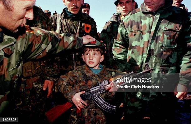 Officers in the Kosovo Liberation Army dress up a young boy as a soldier and give him a gun at a rally February 1999 in Kosovo. Ethnic Albanians in...