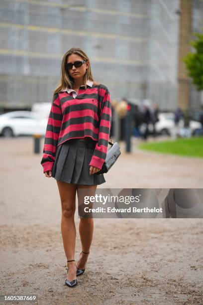 Guest wears black sunglasses, a red and gray striped print pattern polo shirt from Ralph Lauren, a dark gray denim pleated / accordion short skirt, a...