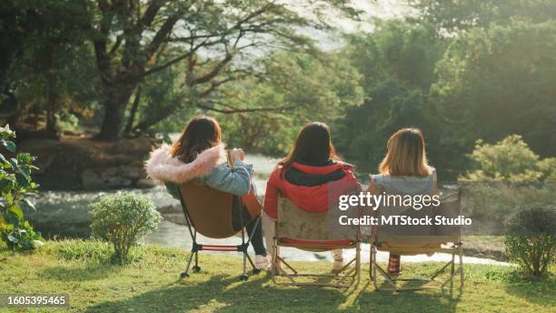 group of happy asian friends talking and drinking a cup of hot coffee for breakfast near stream in vacation with camping caravan at morning. lifestyle travel nature. - human back stock pictures, royalty-free photos & images