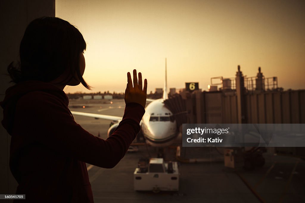 Girl waves goodbye at departing airplane