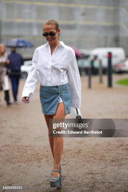 Nikoline Anundsen wears black sunglasses, a white shirt, a pale blue slit / split micro short skirt, a silver rhinestones handbag from Valentino,...