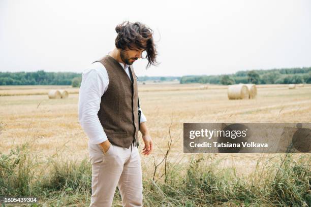 serene mature farmer in stylish summer outfit enjoying solitary stroll by harvested hay field - bartstoppel stock-fotos und bilder