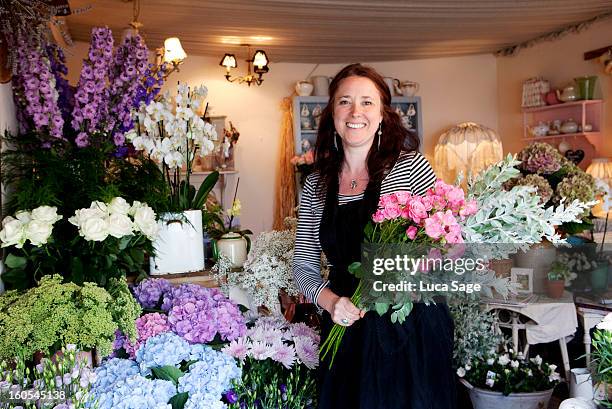 a florist smiles amidst her array of flowers - floristería fotografías e imágenes de stock