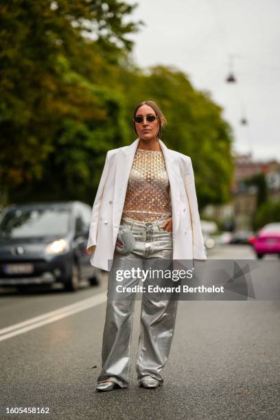 Guest wears black sunglasses, a beige tulle with embroidered gold sequined top, a beige blazer jacket, silver shiny leather large pants, a...