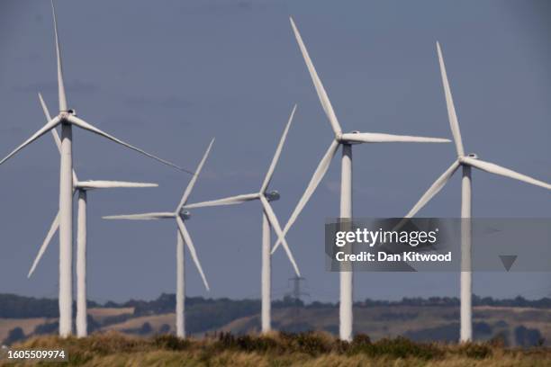 Wind turbines and power lines cut across the landscape of the Romney Marshes on August 10, 2023 in Camber, United Kingdom.