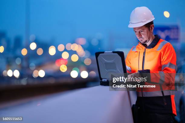 maintain decision-making flexibility to control projects and their impact in construction industry. a male project manager using a laptop computer to follow up and up to date of project task at a bridge construction site. night working, field event. - risikomanagement stock-fotos und bilder