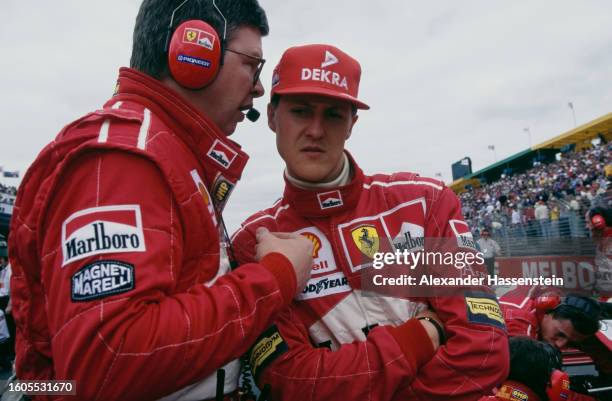 Team official in conversation with German racing driver Michael Schumacher, wearing a red baseball cap and red coveralls, ahead of the Australian...