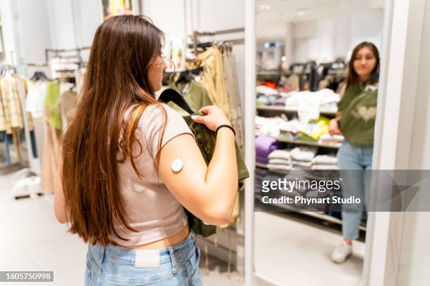 a sixteen year old caucasian girl wearing a diabetes pump in her arm shopping - glucose stockfoto's en -beelden