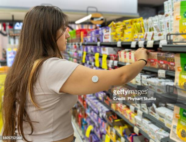 a sixteen year old caucasian girl wearing a diabetes pump in her arm shopping some snack - glucose stockfoto's en -beelden
