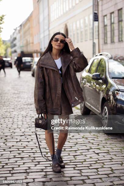 Guest wears a brown mini skirt, brown leather jacket, brown MiuMiu bag, grey socks, brown loafers, and sunglasses outside Remain during the...