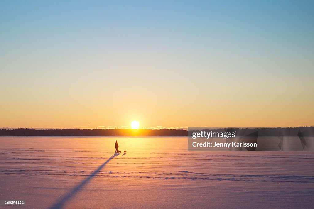 Person with long shadow on frozen lake in sunset