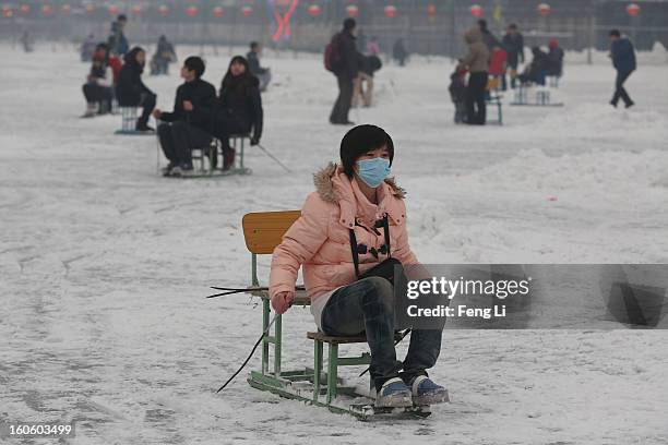 Tourist wearing the mask rides on specially constructed "ice-chairs" on the frozen Houhai Lake during severe pollution on February 3, 2013 in...