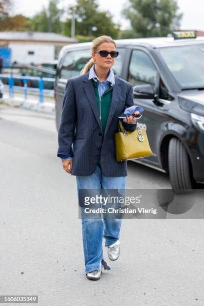 Guest wears navy blazer, green Dior bag, striped button shirt outside Munthe during the Copenhagen Fashion Week Spring/Summer 2024 on August 10, 2023...