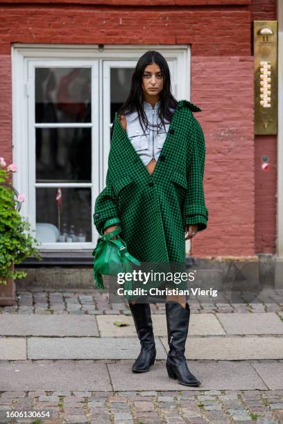 Guest wears green checkered coat, bag, black cowboy boots, cropped top outside Baum und Pferdgarten during the Copenhagen Fashion Week Spring/Summer...