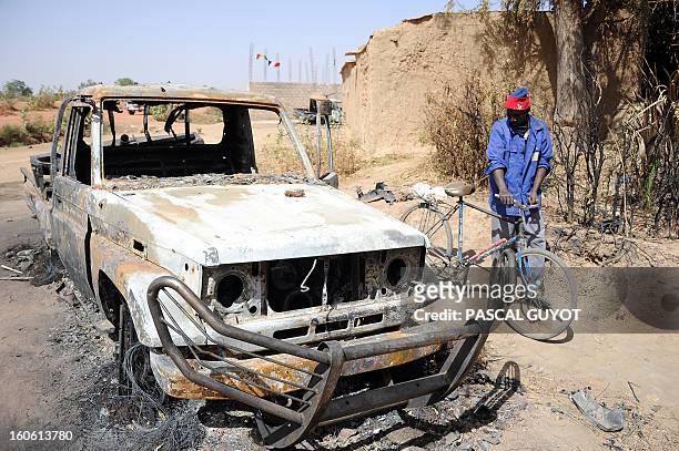 Man stands next to a bicycle past a burnt-out wreck of a vehicle, allegedly used by Islamists, following a major air strike, on February 3, 2013 in...