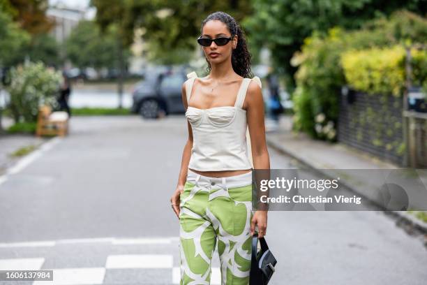 Jamilla Strand wears creme white top, black bag, pants with green white pattern outside Stine Goya during the Copenhagen Fashion Week Spring/Summer...