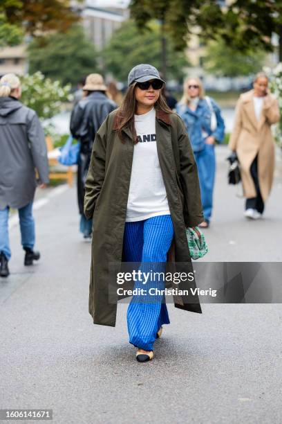 Guest wears grey cap, green coat, blue white striped pants, Jil Sander shirt outside Stine Goya during the Copenhagen Fashion Week Spring/Summer 2024...