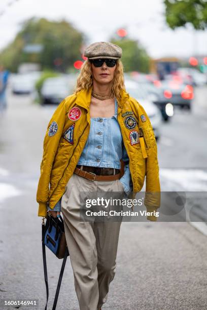 Elina Halimi wears baker boy hat, yellow bomber jacket with patches, Celine bag, beige pants outside Stine Goya during the Copenhagen Fashion Week...