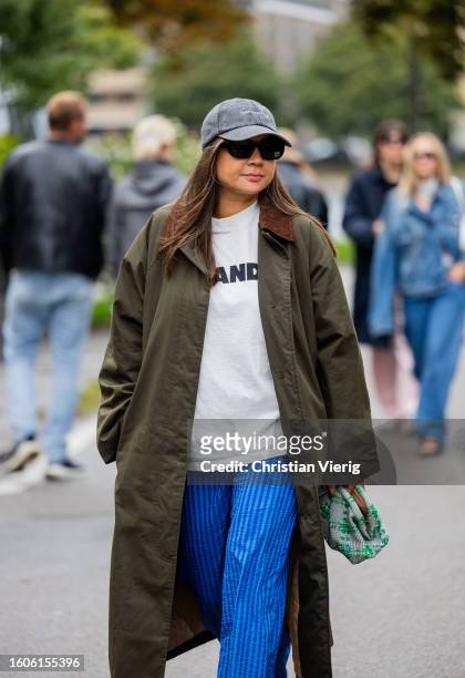 Guest wears grey cap, green coat, blue white striped pants, Jil Sander shirt outside Stine Goya during the Copenhagen Fashion Week Spring/Summer 2024...