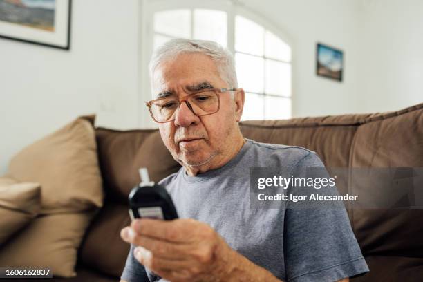man looking at glucometer result at home - glucose stockfoto's en -beelden