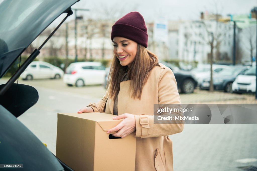 Ritratto di una donna felice che porta una scatola con il personale che ha comprato in macchina