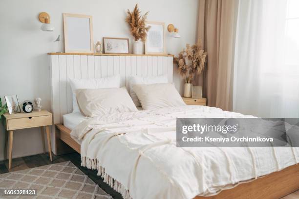 simple bulb lamp on a rope hanging above bed with white bedclothes, books and gold fern leaf on an end table in white bedroom interior - confort at hotel bedroom stock pictures, royalty-free photos & images