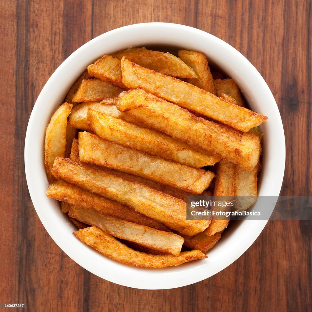 Thick-cut potato fries in a bowl on wood grain