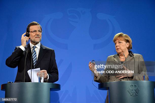 German Chancellor Angela Merkel and Spain's Prime Minister Mariano Rajoy adjust their earpieces as they addresses a press conference at the...
