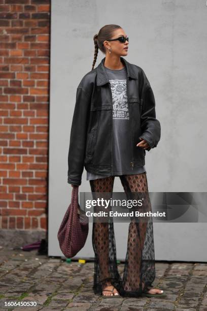 Guest wears black sunglasses, a gray with white print pattern oversized t-shirt, a black shiny leather bomber jacket, black lace print pattern tulle...