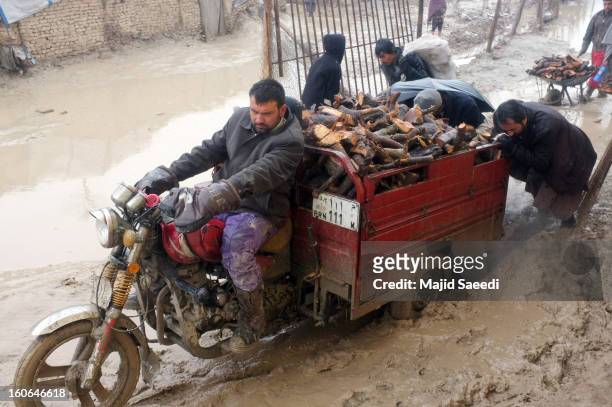 Internally displaced Afghans transport firewood, donated by Danish Refugee Council , through heavy reain and thick mud on a motorcycle-drawn trailer,...