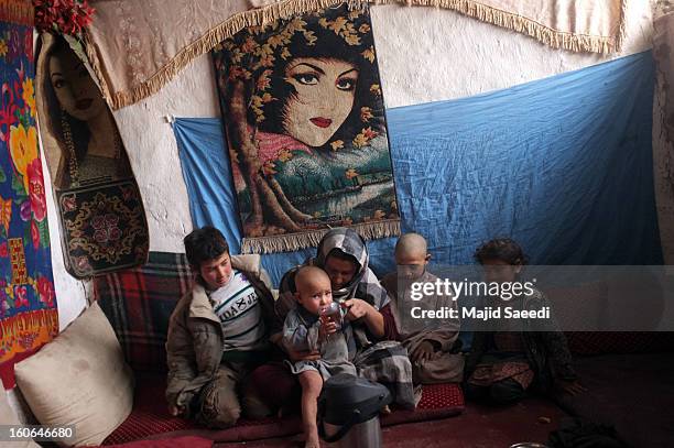 Displaced Afghan family sit around their mother as she helps a child drink at Chamand babrak Camp, on February 3, 2013 in Kabul, Afghanistan....