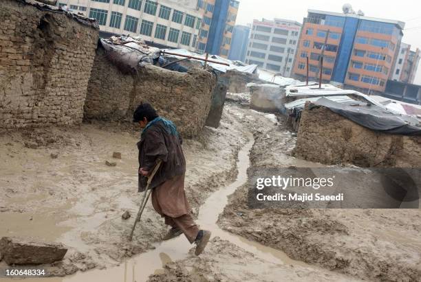 An internally displaced Afghan on crutches makes his way over a rain-filled, muddy ditch at Chamand babrak Camp, on February 3, 2013 in Kabul,...