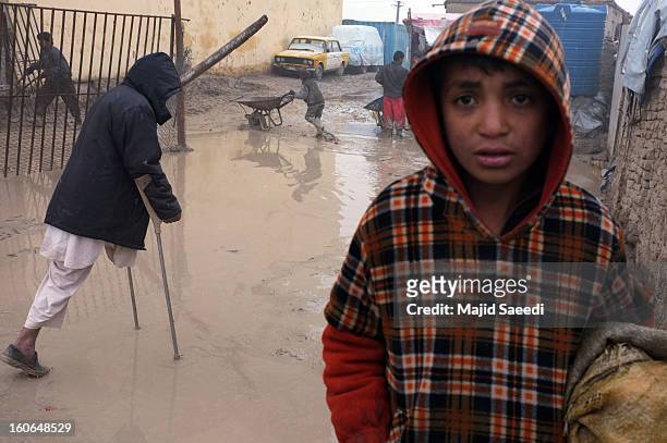 One-legged war veteran uses crutches in the rain as internally displaced Afghans wait to receive aid donations from the Danish Refugee Council at...