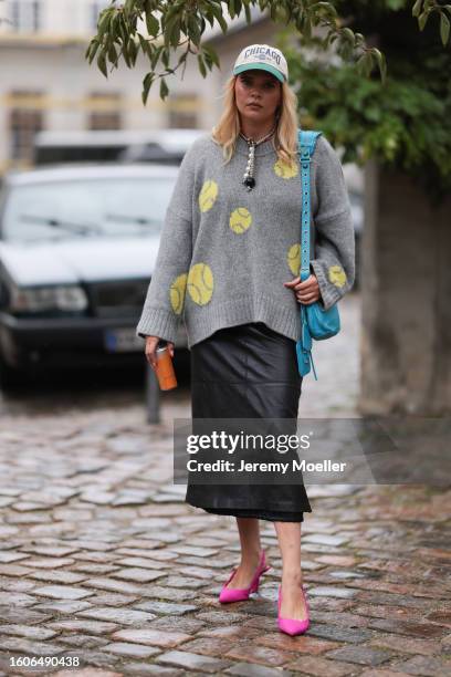 Guest seen outside Marimekko show wearing grey Chicago cap, big pearl necklace, grey oversized sweater with yellow basketballs embroided, black midi...