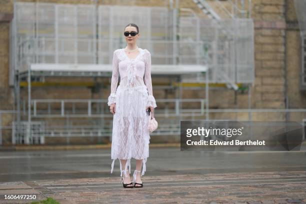 Guest wears black sunglasses, a white lace flower embroidered pattern ruffled V-neck / long sleeves / long dress, a pale pink braided fabric handbag,...